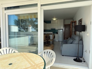 Un balcon avec une porte vitrée, une table à manger avec des chaises, un canapé gris et une lampe sur pied.