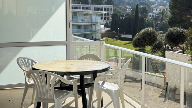 Un balcon avec une table et des chaises, donnant sur un quartier résidentiel avec des maisons et des arbres.