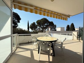 A balcony with a table and chairs, a striped awning, and a view of trees and buildings. - Agi Almadraba 2101 Apartamento for rent in Roses Girona. (Rosas / Roses)