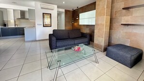 A modern living room with a glass coffee table, grey sofa, and a small ottoman. - Agi Drugstore AD Apartamento for rent in Roses Girona. (Rosas / Roses)