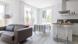 A modern kitchen with a dining area, large windows, and a grey sofa. - Apartment with private garden and communal jacuzzi, next to the beach and the center (Roses)