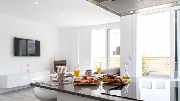 A modern kitchen with a breakfast setup, including croissants, orange juice, and a bottle of olive oil. - Apartment with private garden and communal jacuzzi, next to the beach and the center (Roses)