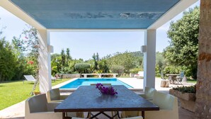 An outdoor patio with a pool, white furniture, and a view of the surrounding garden and hills. - Private retreat with pool near the sea (Son Servera)