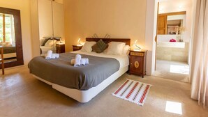 A bedroom with a large bed, two bedside tables with lamps, a wooden headboard, and a view into the bathroom. - Private retreat with pool near the sea (Son Servera)