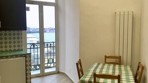 Un coin repas avec une nappe à carreaux, des chaises en bois, un petit espace cuisine avec un placard, et une vue sur le paysage urbain à travers une porte vitrée.