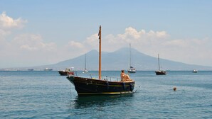 Un bateau avec deux personnes à bord, ancré dans une eau calme, avec plusieurs autres bateaux et une montagne en arrière-plan.