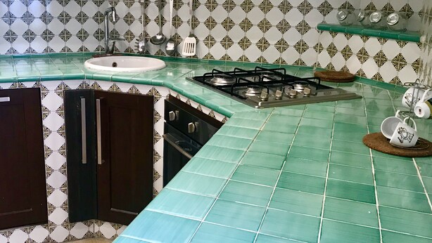 Une cuisine avec un plan de travail recouvert de carreaux verts, une cuisinière à gaz, un évier et des meubles de rangement en bois foncé.