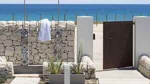 Eine Steinsäule mit einem Handtuch an einem Haken, eine hölzerne Bank und eine Tür, die Blick auf den Strand bietet.