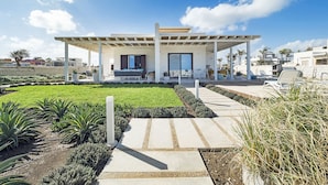Ein modernes Haus mit überdachter Terrasse, einem gepflegten Garten und blauem Himmel.