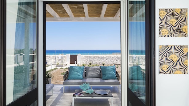 Ein moderner Außenbereich zum Sitzen mit einer Couch und Couchtisch, mit Blick auf einen Strand.