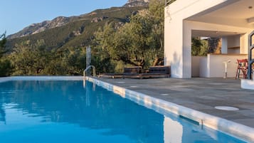 A swimming pool with a mountain backdrop, a modern outdoor seating area, and a stone wall.