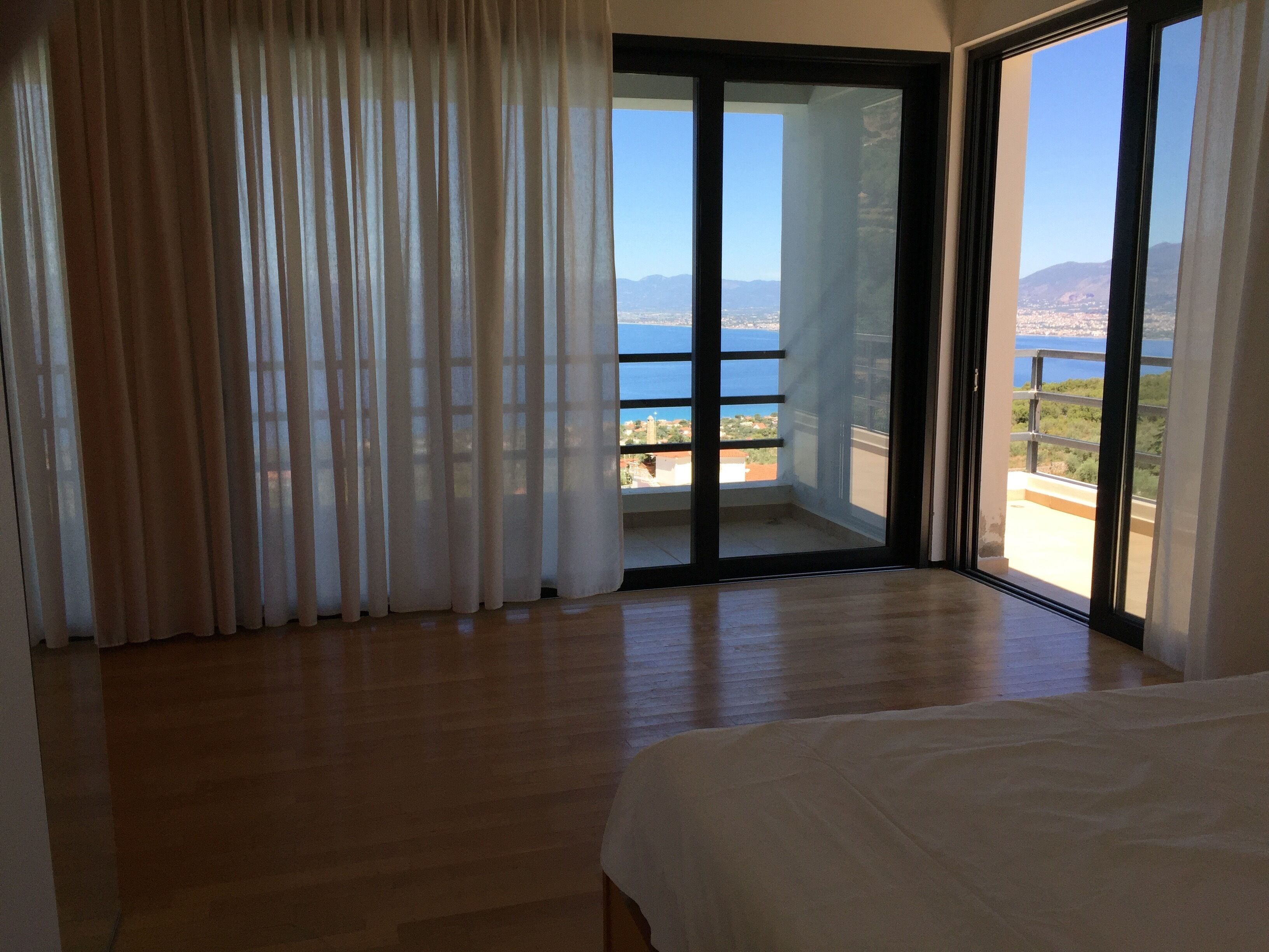 A room with a large sliding glass door leading to a balcony with a view of the sea and mountains.