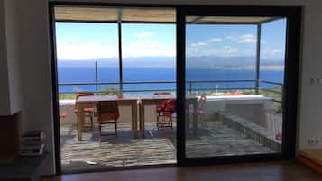 A balcony with a view of the sea, a table, and chairs.