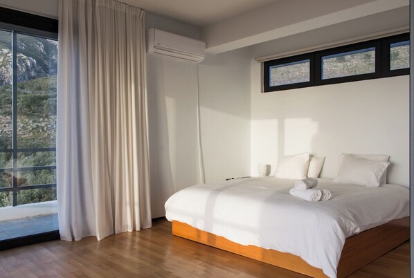 Une chambre à coucher moderne avec un grand lit, une fenêtre avec des rideaux et une vue sur l’extérieur.