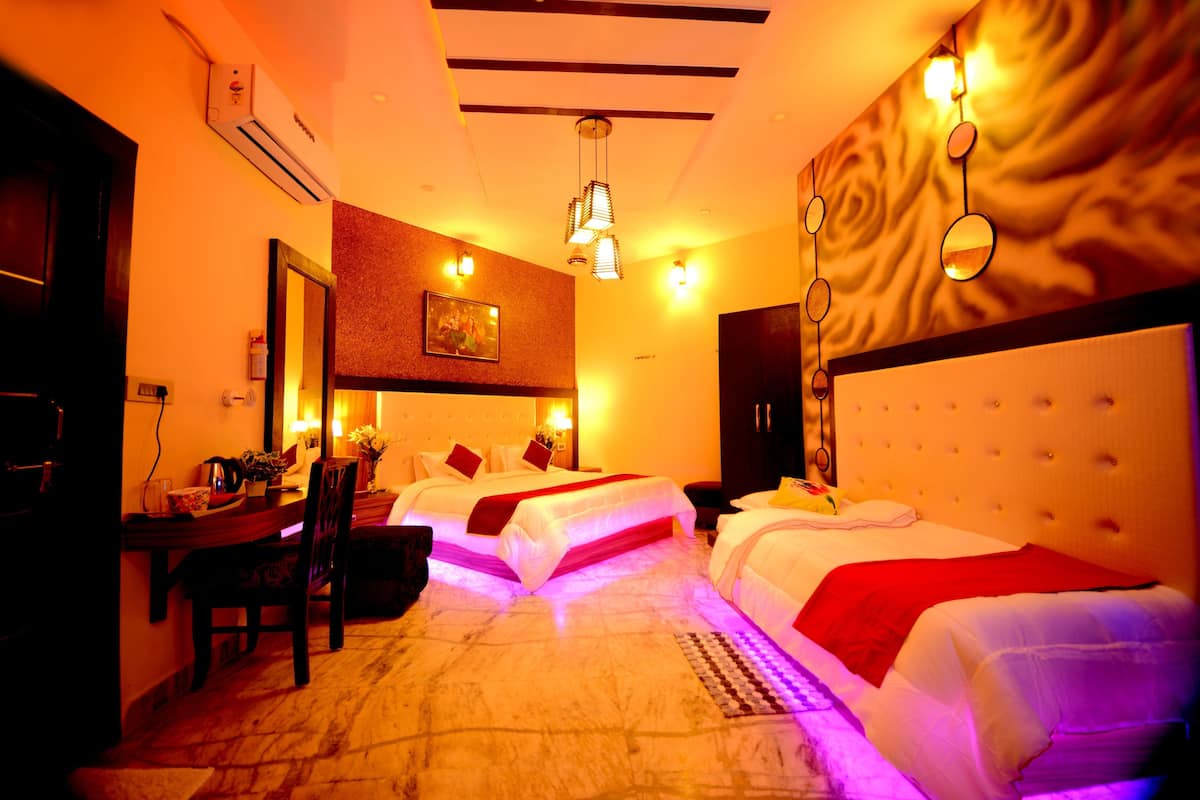 A hotel room with two beds, a desk, and a chair. There is a painting on the wall and a ceiling fan.
