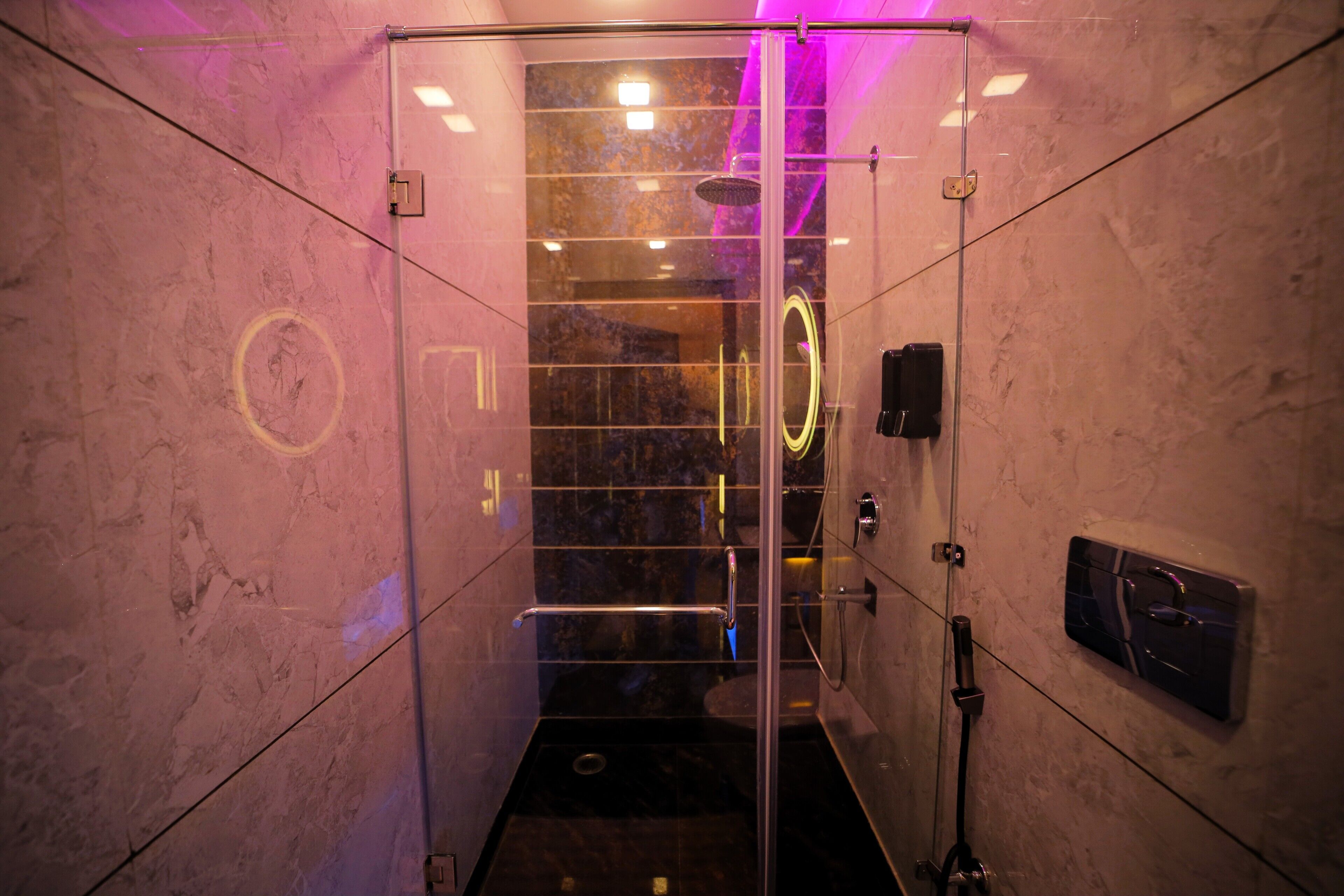 A glass-enclosed shower area with a marble wall, a handheld showerhead, and a handheld massager on the wall.