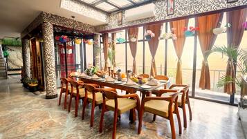 Comedor con una mesa larga dispuesta para varias personas, ventanas amplias con cortinas y vista a zonas verdes.