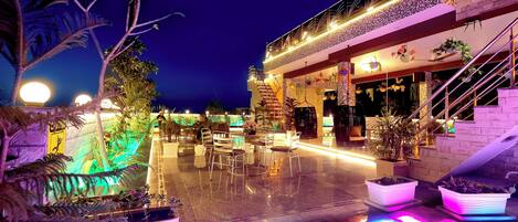 A well-lit outdoor area with a pool, seating, and potted plants.
