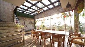 A dining area with a large table and chairs, a staircase with a railing, and a view through a glass ceiling. - Aman Homestay a Boutique Hotel (Agra)