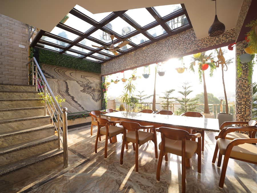 Un área de comedor con una gran mesa y sillas, una escalera con barandilla y vistas a través de un techo de cristal.