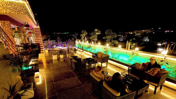 An outdoor seating area with wicker furniture and a pool with illuminated edges. - Aman Homestay a Boutique Hotel (Agra)