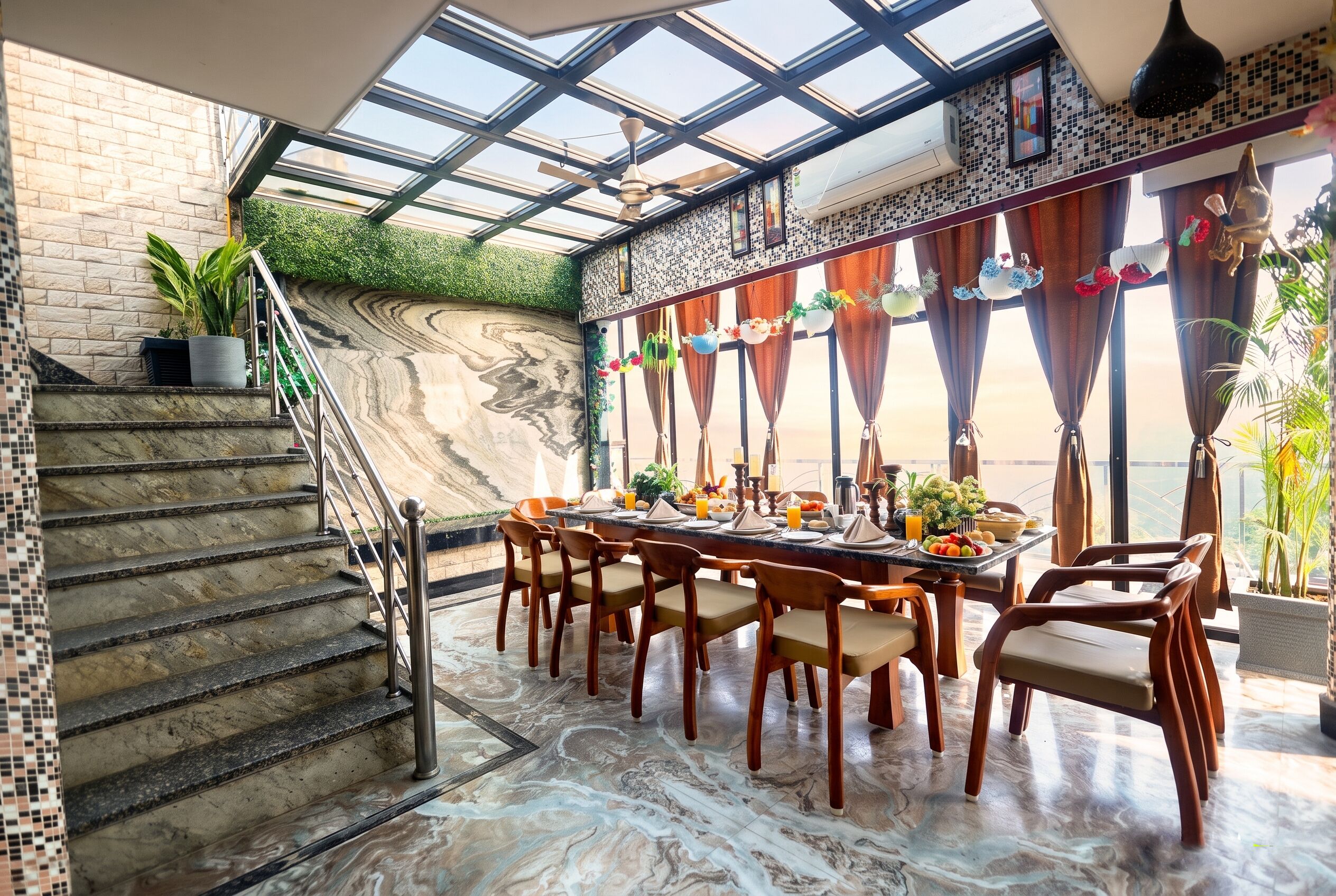 A dining area with a marble floor, a staircase with a glass railing, and a view of the outdoors through large windows.