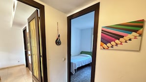 A hallway with a bed, a door with a decorative glass panel, and a colorful abstract painting on the wall. - Agi Can Parramon A Apartamento for rent in Roses Girona. (Rosas / Roses)