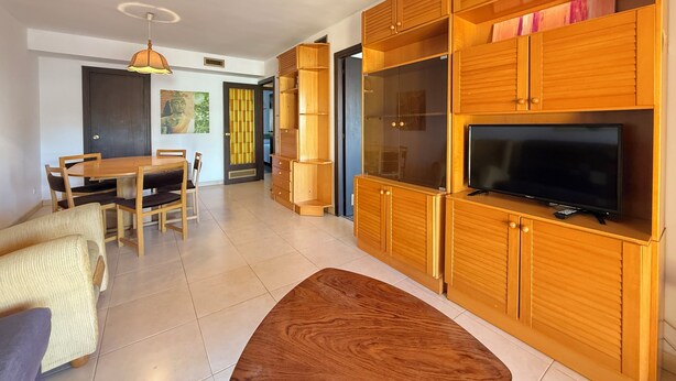 A modern living room with a wooden TV stand, a flat-screen TV, and a dining area with a wooden table and chairs. - Agi Can Parramon A Apartamento for rent in Roses Girona. (Rosas / Roses)