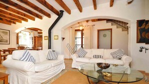 A living room with two white sofas, a glass coffee table, wooden beams, a staircase, and a dining area with wooden furniture. - Can Teulada, private pool Pollensa 12 persons (Pollensa)