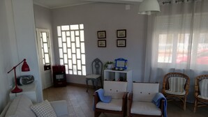 A living room with a sofa, two armchairs, a red lamp, a radiator, a window with a grid pattern, and framed pictures on the wall.