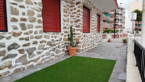 A stone building with red shutters, a potted cactus, and a green artificial turf area.