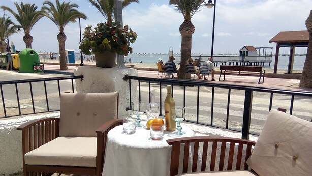 A table set with a white tablecloth, two wooden chairs, and a potted plant.