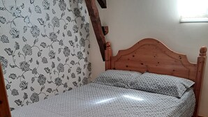 A wooden bed with a patterned bedspread and pillows, a wooden headboard, and a floral wallpaper pattern on the wall. - Rose Gite Le Cosquer Saint Connec (Saint-Connec)