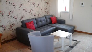 A living room with a grey sofa, red cushions, a white coffee table, and floral wallpaper. - Rose Gite Le Cosquer Saint Connec (Saint-Connec)
