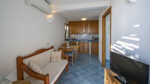 Un espacio habitable pequeño con sofá, televisión, kitchenette y zona de comedor.