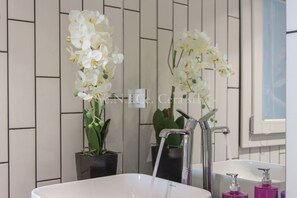 Un bagno con un lavandino bianco, un rubinetto moderno e due piante di orchidea.