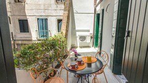 Un petit balcon extérieur avec une table et des chaises, un pot de fleurs et une vue sur un immeuble avec une porte verte.