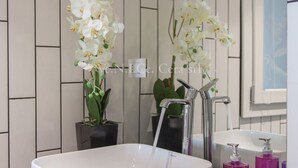 Une salle de bain avec un lavabo blanc, un robinet moderne et deux plantes orchidées.