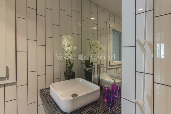 A modern bathroom with a white sink, black countertop, and white tiled walls.