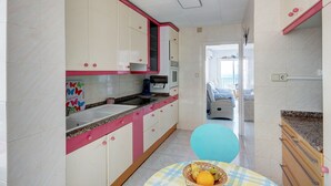 A kitchen with white cabinets, a sink, and a countertop. There is a table with a basket of fruit. - STA. MONICA 3ºA - Apartment for 6 people in Rosas / Roses (Roses)