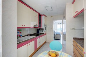 A kitchen with white cabinets, a sink, and a countertop. There is a table with a basket of fruit.