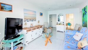 A living room with a TV, white cabinets, a glass coffee table, a blue sofa, and a painting of a beach scene. - STA. MONICA 3ºA - Apartment for 6 people in Rosas / Roses (Roses)