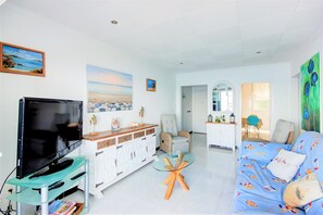 A living room with a TV, white cabinets, a glass coffee table, a blue sofa, and a painting of a beach scene. - STA. MONICA 3ºA - Apartment for 6 people in Rosas / Roses (Roses)