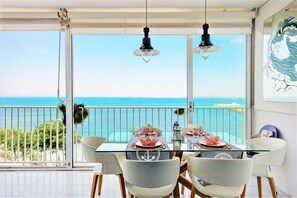 A dining area with a table set for four, overlooking a balcony with a view of the sea.