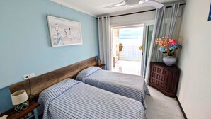 A hotel room with two beds, a ceiling fan, a painting, a vase of flowers, and a view of the sea. - STA. MONICA 3ºA - Apartment for 6 people in Rosas / Roses (Roses)