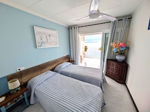 A hotel room with two beds, a ceiling fan, a painting, a vase of flowers, and a view of the sea. - STA. MONICA 3ºA - Apartment for 6 people in Rosas / Roses (Roses)