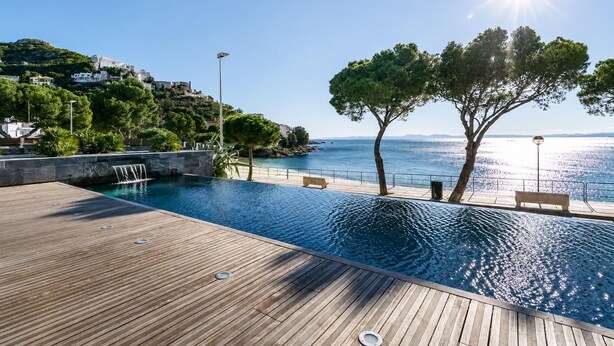 A wooden deck with a swimming pool, benches, and a view of the sea. - Beachfront two-bedroom apartment with sea views in Canyelles Petites (Roses)