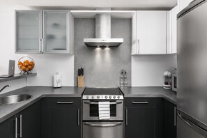 A modern kitchen with a stainless steel stove, oven, and refrigerator, dark cabinetry, and a grey backsplash.