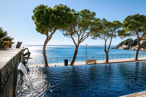 A pool with a view of the sea, surrounded by trees and a bench.