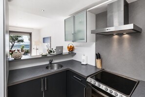 Eine moderne Küche mit Einbauofen, Spüle aus Edelstahl und Meerblick durch ein Fenster.